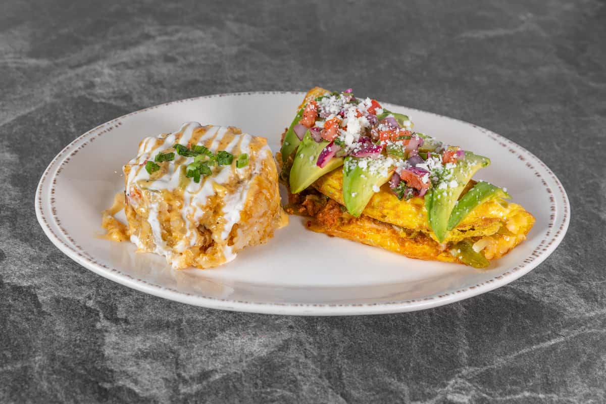 Two slices of toasted bread topped with avocado, colorful vegetables, fresh herbs, and creamy sauce, served on a white plate with a side of seasoned salad.