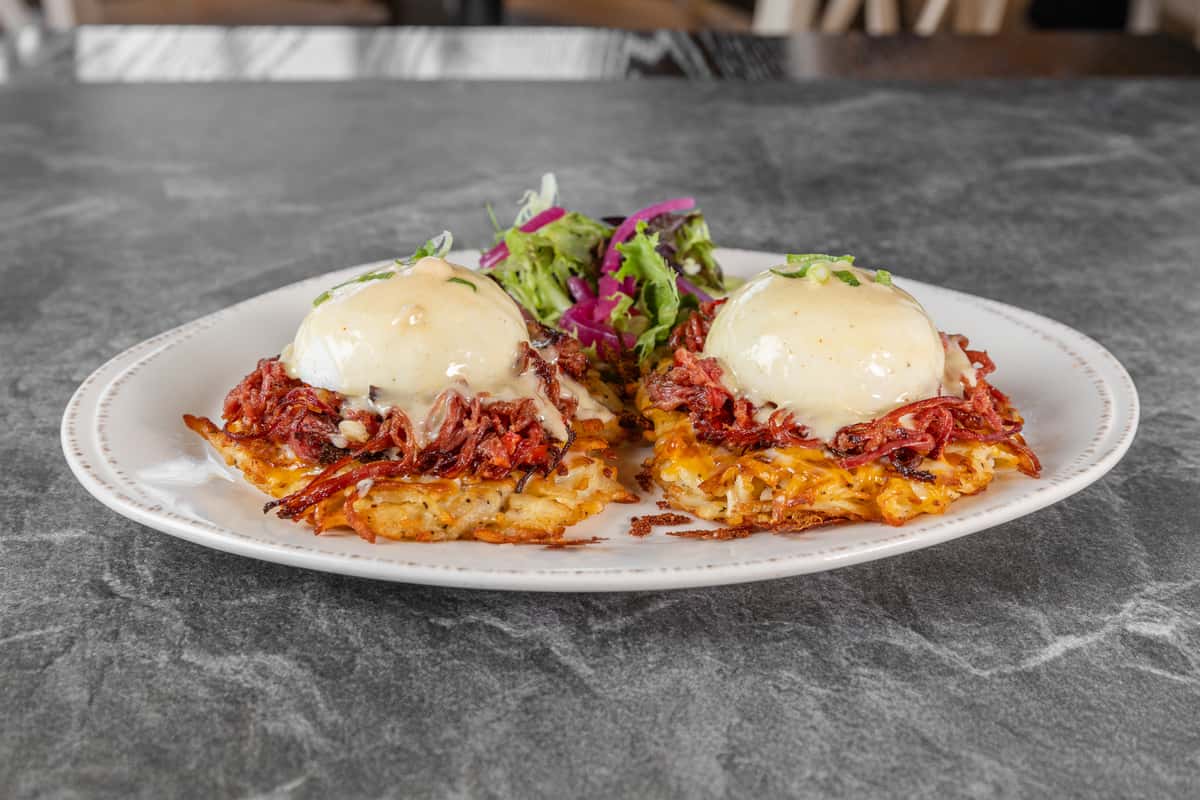Two servings of eggs Benedict topped with poached eggs and creamy hollandaise sauce, served on a crispy golden base with fresh greens and colorful garnishes.