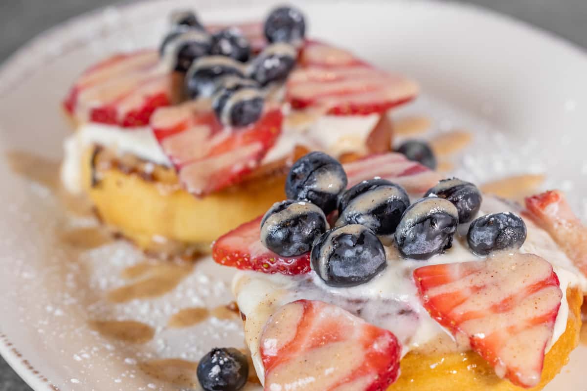 Slices of toasted bread topped with strawberries, blueberries, and a creamy spread, served as a colorful breakfast dish.