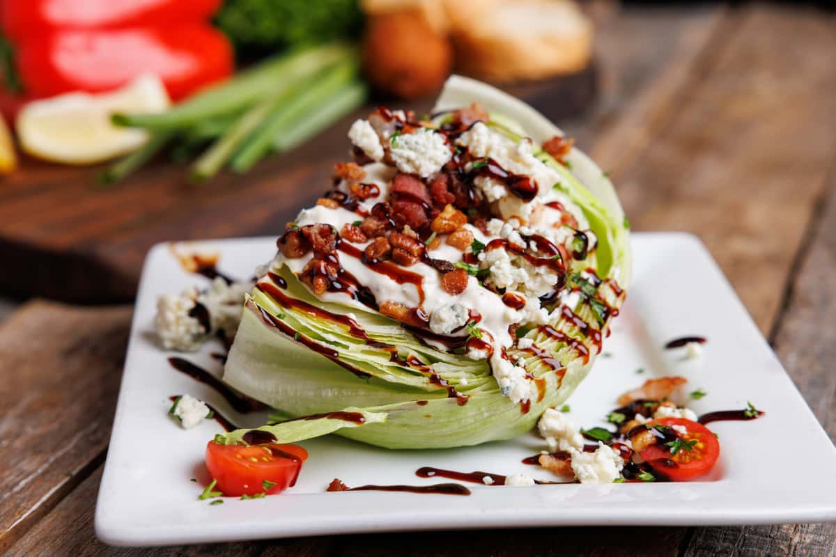 Iceberg wedge salad topped with creamy dressing, crispy bacon bits, crumbled blue cheese, and balsamic glaze, served on a modern restaurant appetizer plate