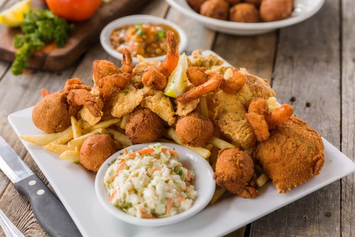 A fried seafood platter with fried shrimp, fish and hushpuppies with a side of coleslaw and french fries