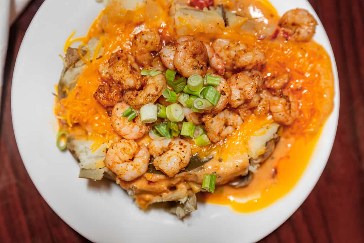Loaded baked potato topped with seasoned shrimp, shredded cheddar cheese, green onions, and a creamy orange sauce.