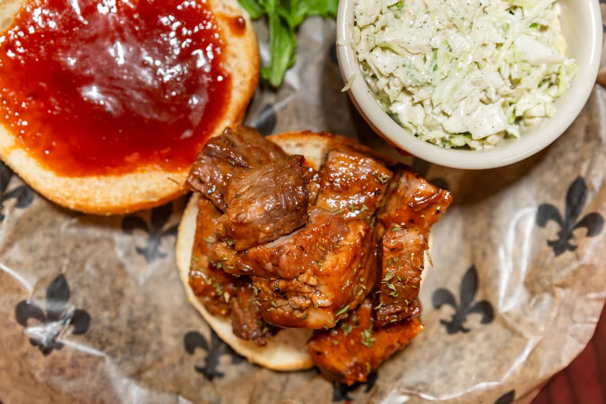 BBQ beef sandwich on a bun with barbecue sauce, served with a side of creamy coleslaw in a small bowl.