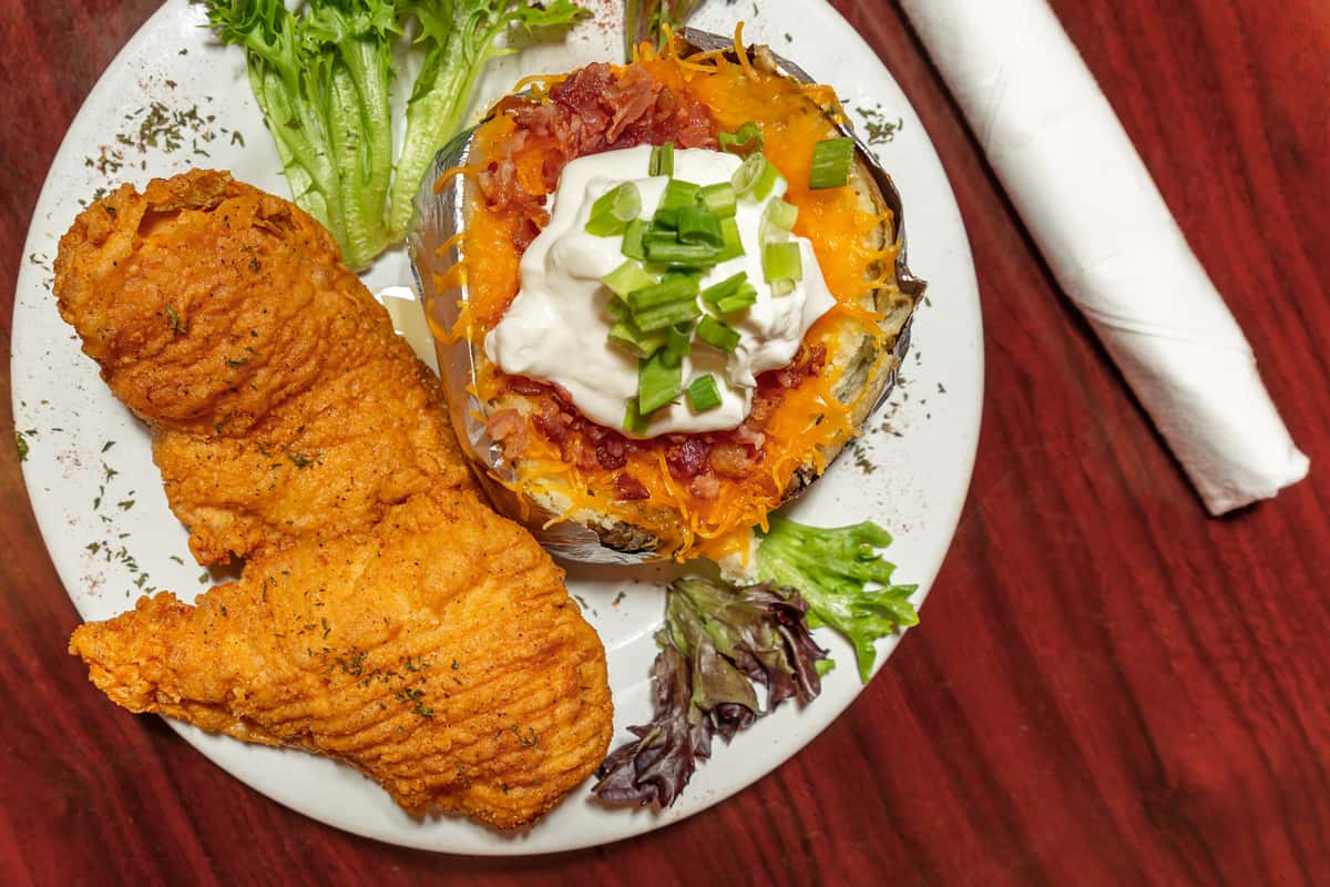 Crispy fried fish fillets served with a loaded baked potato topped with cheese, bacon, sour cream, and green onions.