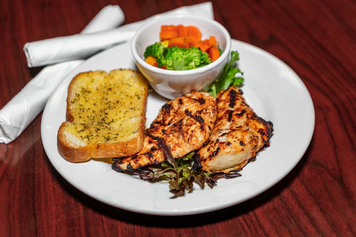 Grilled chicken breast served with garlic toast and a side of steamed broccoli and carrots.