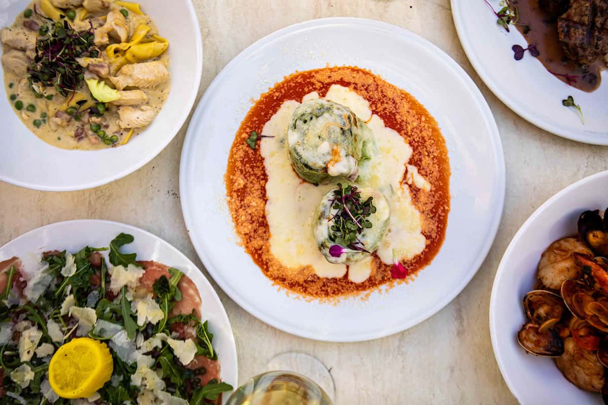 An overhead view of a classic Italian pasta dish served in a vibrant tomato sauce, topped with creamy cheese and fresh herbs. Surrounded by additional plates, the setting suggests a shared, family-style meal full of authentic flavors and comforting appeal.