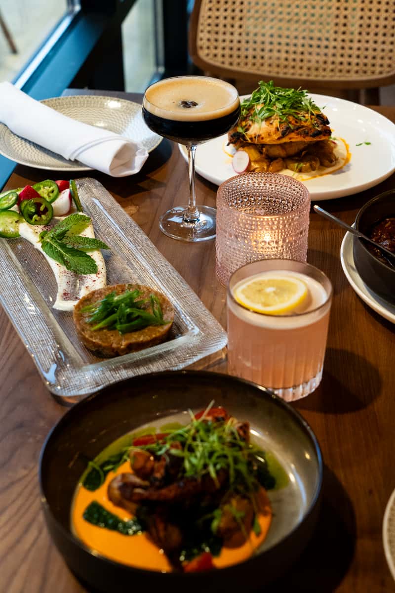 A table set with various elegant Mediterranean dishes, including appetizers, a cocktail garnished with lemon, and a softly lit candle