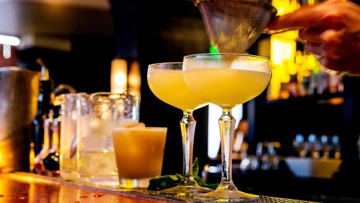 Bartender pouring a bright yellow cocktail into a glass at a bar.