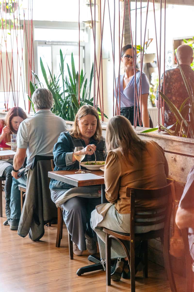 Interior shot of Abejas restaurant. Customers dine in a naturally-lit dining room, separated by wooden staves.