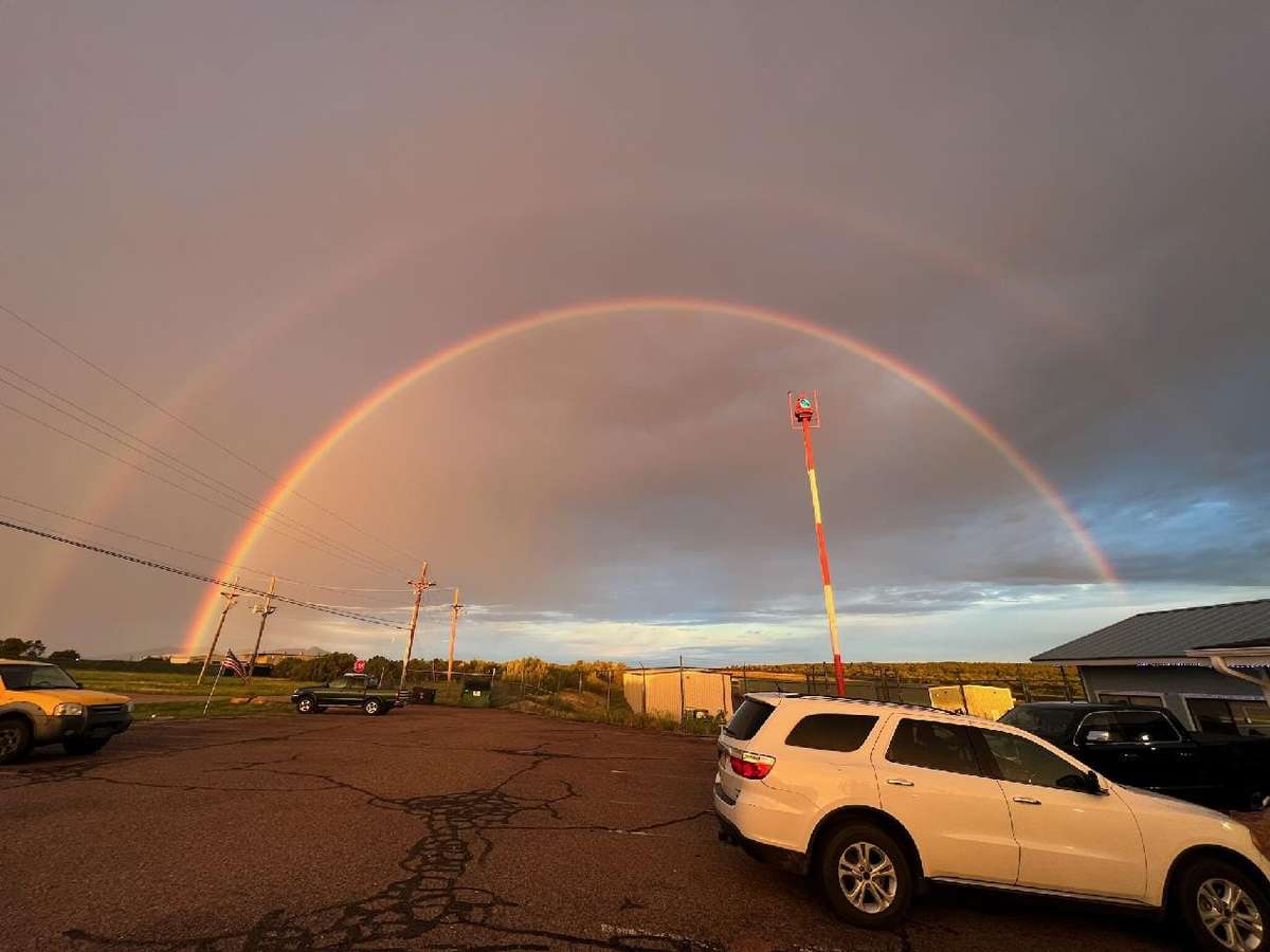 Vibrant double rainbow arches over the parking lot of Crosswinds Restaurant in Payson, Arizona, during golden hour after a storm.