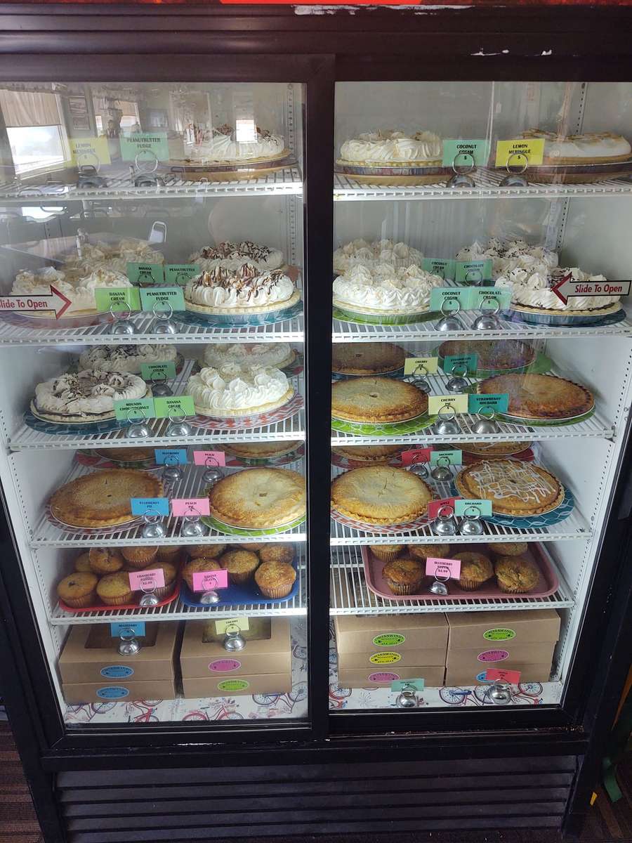 Refrigerated display case filled with assorted homemade pies, cream-topped desserts, and muffins at Crosswinds Restaurant, each labeled with colorful tags.