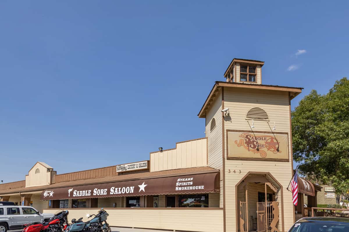 Exterior of Saddle Sore Saloon with brown awning, tower sign, motorcycles parked, and a clear blue sky.