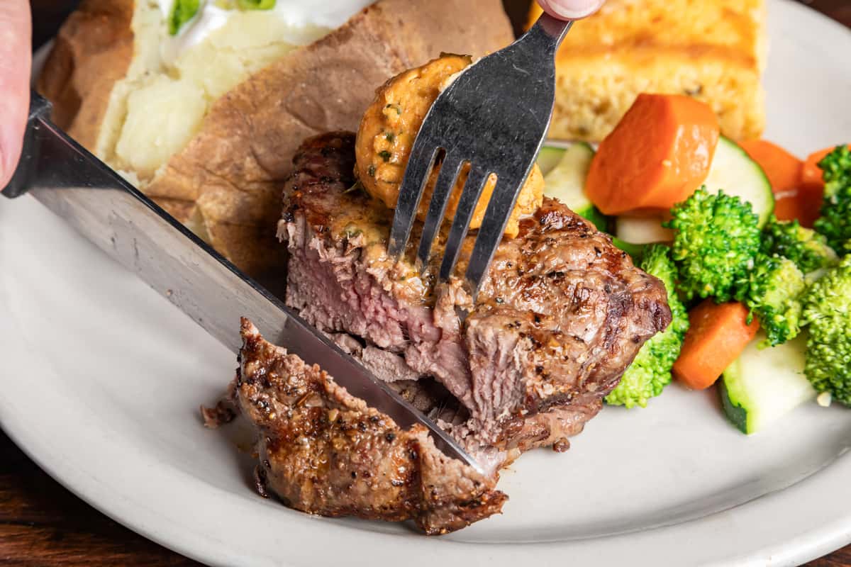 Juicy grilled steak topped with seasoned butter, served with a baked potato, cornbread, and mixed steamed vegetables.