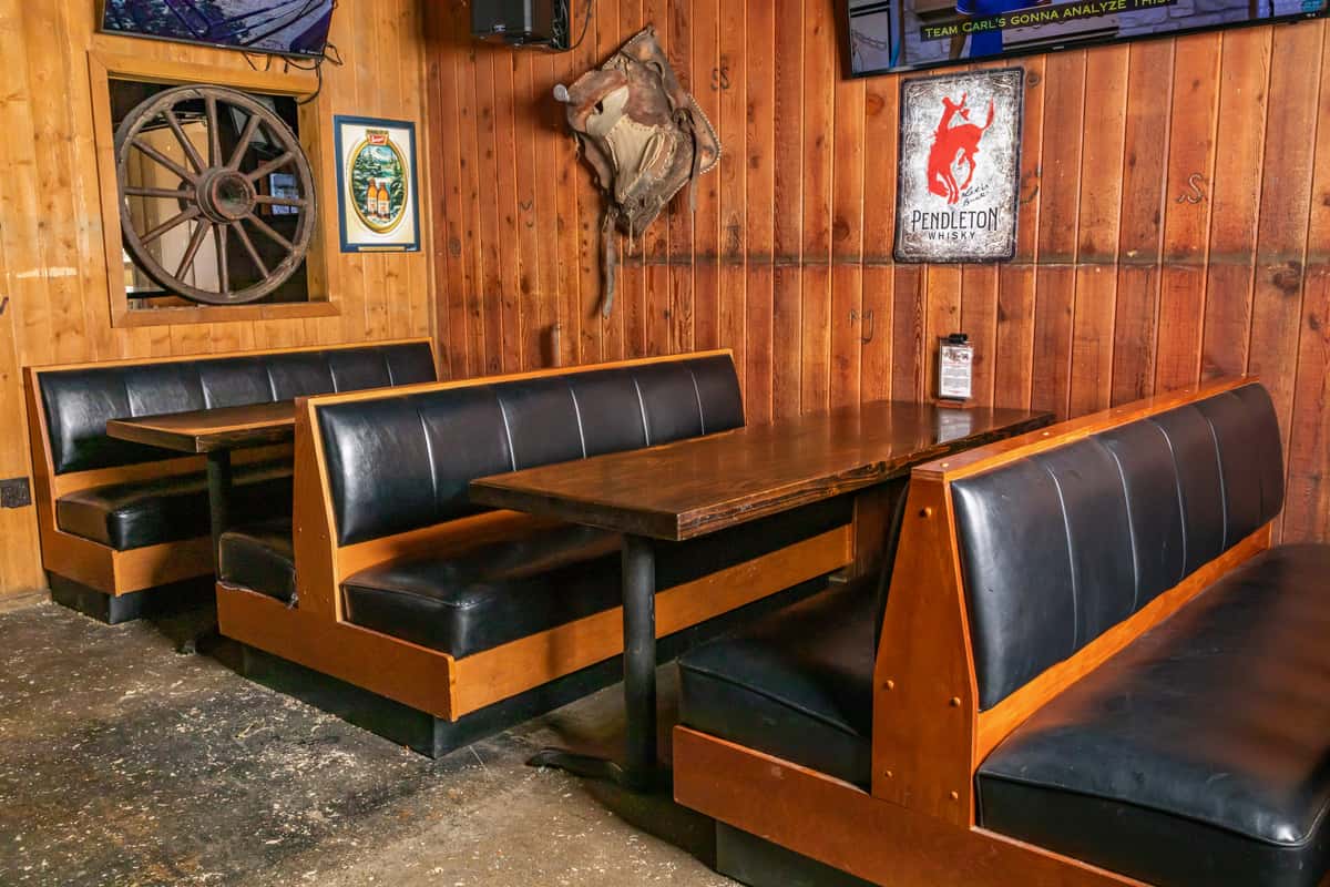 Wood-paneled dining area with black leather booths and western decor including a saddle, wagon wheel, and Pendleton Whisky sign.