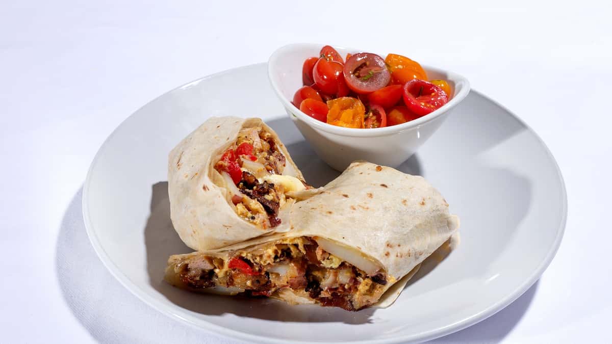 liced breakfast burrito on a white plate, served with a small bowl of cherry tomatoes