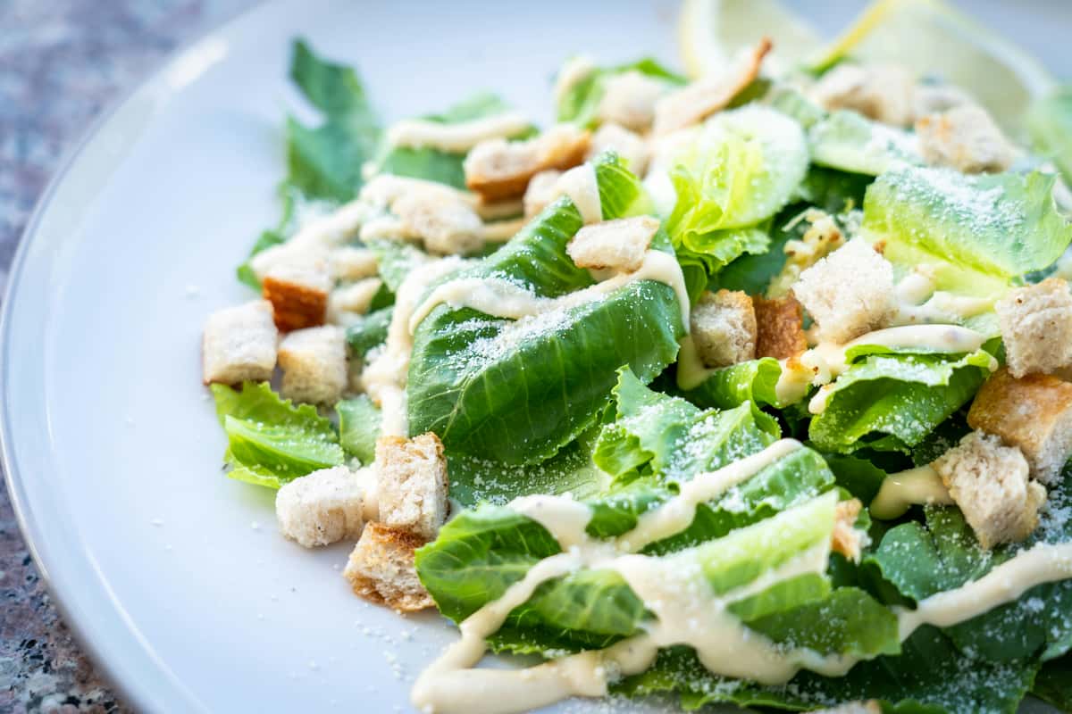 Caesar salad with romaine lettuce, croutons, grated parmesan, and creamy dressing, served with lemon wedges on a white plate.