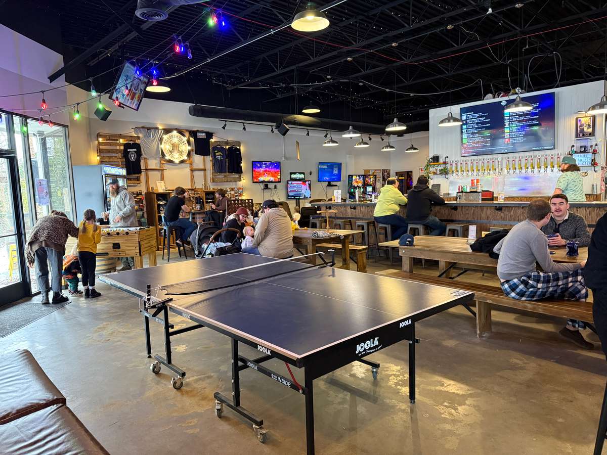 Inside the Schoolhouse Brewing taproom in Marietta, GA, with a ping pong table, the tap wall and bar, and guests at wooden tables