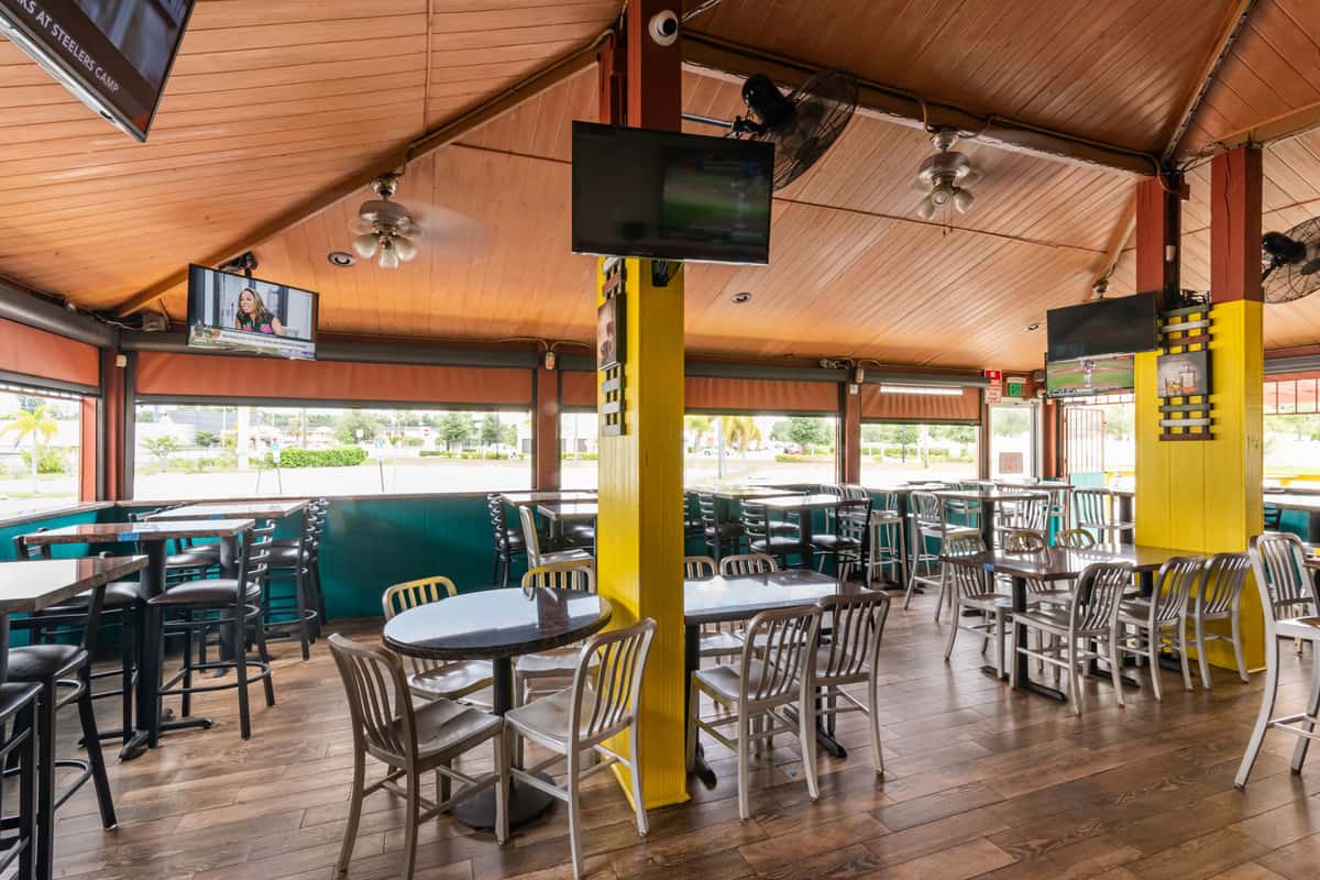 Spacious Caribbean restaurant interior with wood-paneled ceiling, vibrant yellow pillars, flat-screen TVs, and casual metal seating—ideal for relaxed dining and enjoying Latin American cuisine in a bright, tropical-inspired setting.
