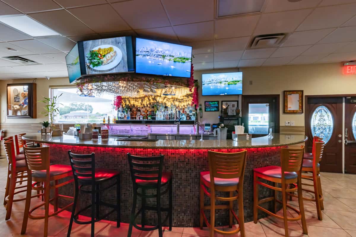 Colorful Caribbean bar with ambient red and purple LED lighting, curved granite countertop, wood barstools, and overhead TVs—inviting nightlife atmosphere for tropical cocktails and Latin fusion dining.