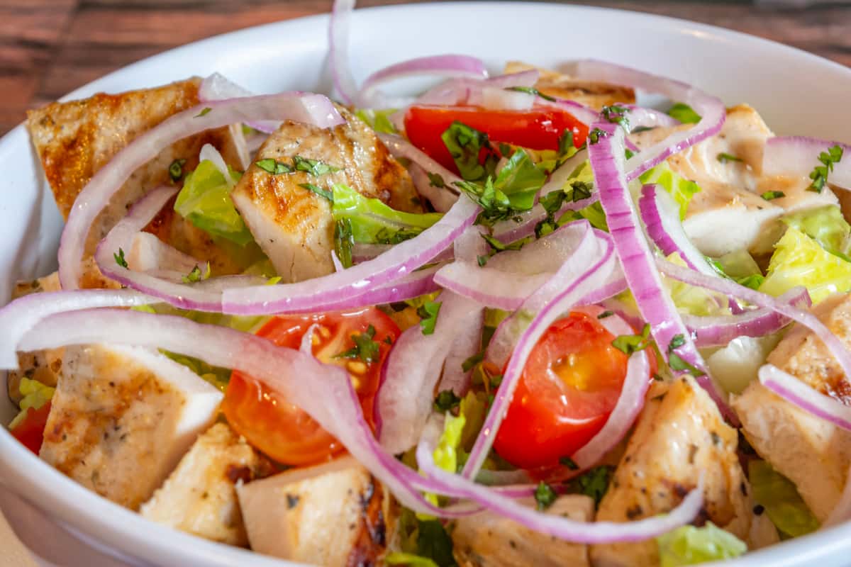 Close-up of grilled chicken salad with romaine lettuce, cherry tomatoes, red onions, and fresh cilantro—vibrant and healthy Caribbean-style dish packed with flavor.