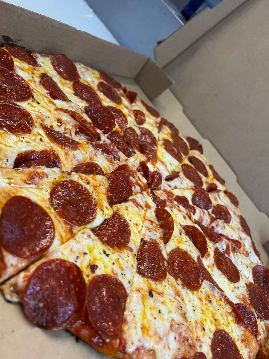 Freshly baked pepperoni pizza in a box, topped with melted cheese and evenly spaced pepperoni slices.