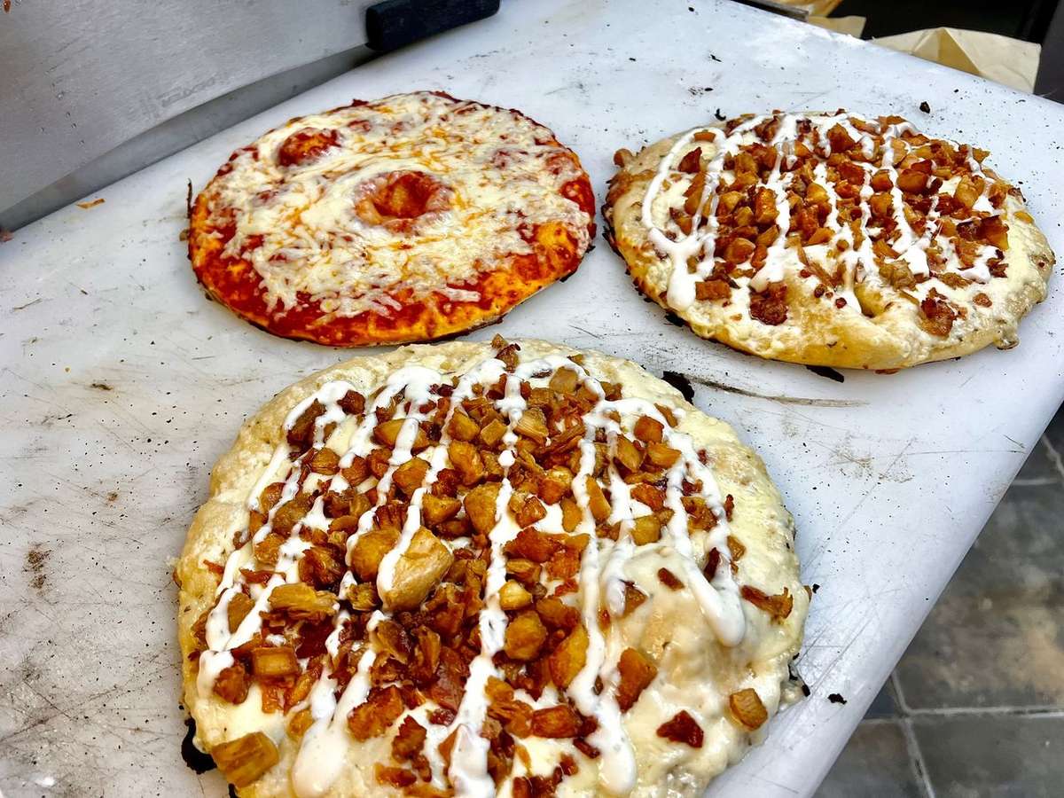 Three freshly prepared personal pizzas on a cutting board, two topped with chicken and ranch, one with melted cheese only.
