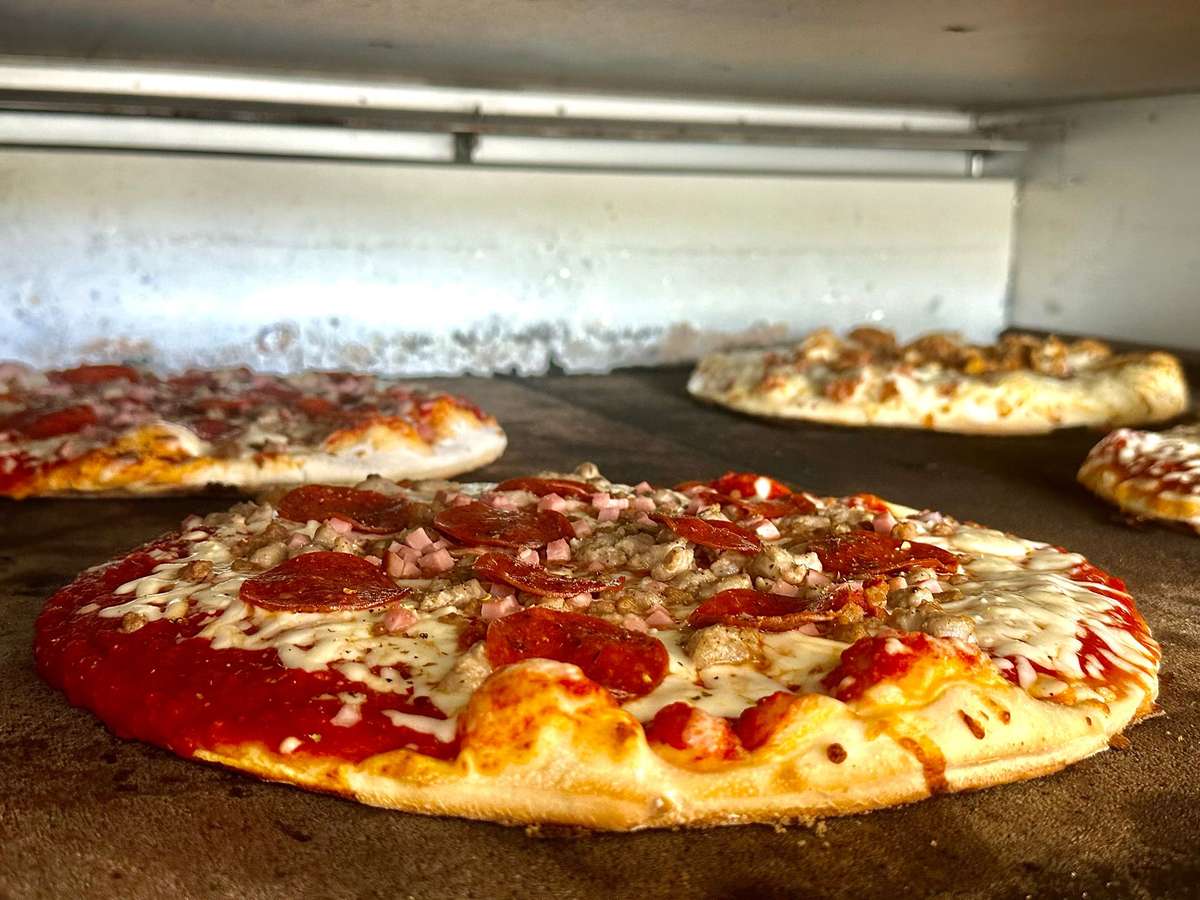 Assorted pizzas baking in a stone oven, featuring pepperoni, sausage, and melted cheese on golden crusts.