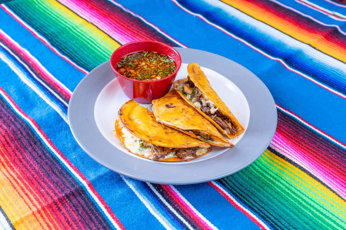 Three Quesabirria tacos on a round plate with salsa on the side