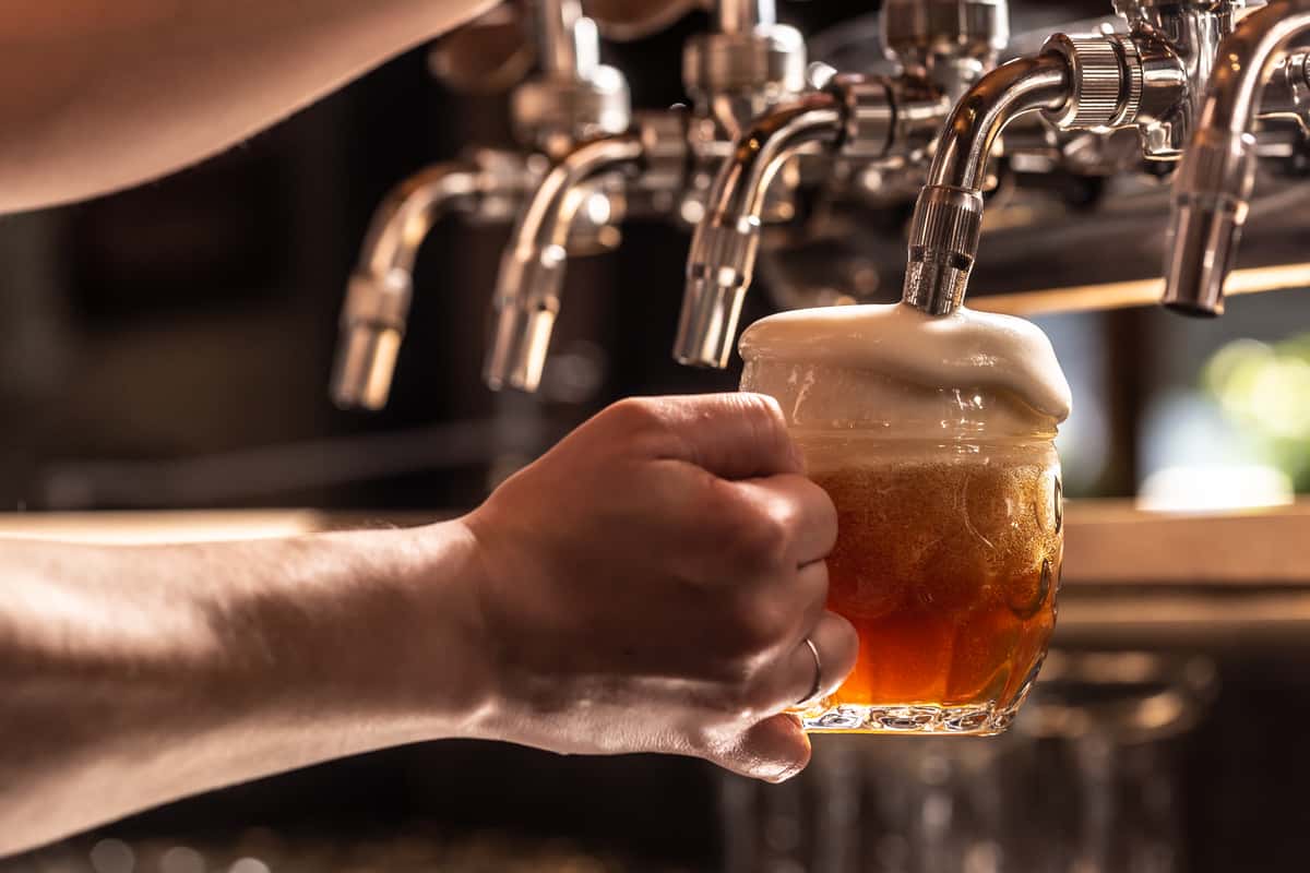 Person holding a glass mug under a beer tap while it is being filled.