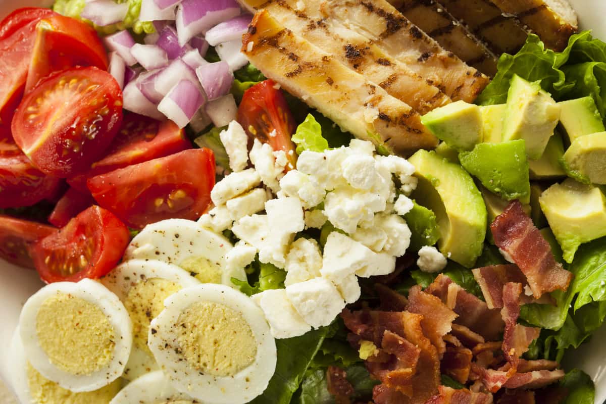 Closeup of a cobb salad with boiled eggs, tomato, red onion, and bacon