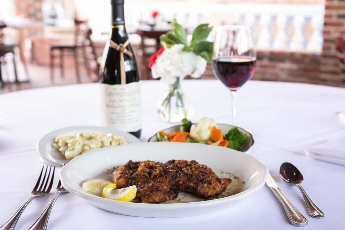 elegantly plated entree with glass of wine and bouquet of flowers
