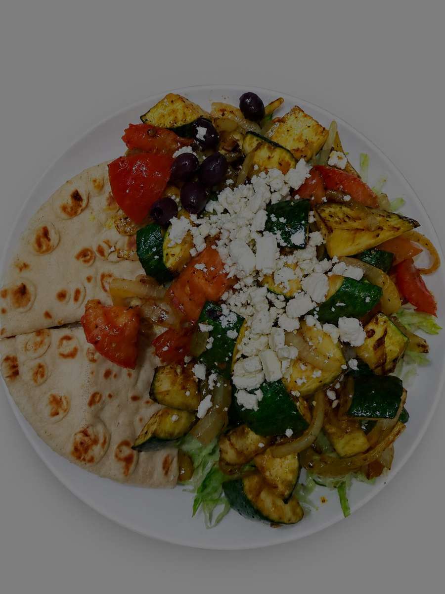 Mediterranean grilled vegetable platter with zucchini, tomatoes, onions, feta cheese, Kalamata olives, and warm pita bread served over fresh lettuce.