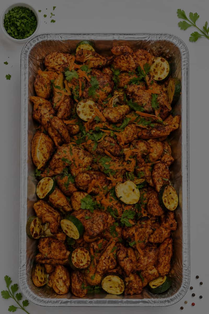 Large catering tray of grilled Mediterranean chicken with roasted zucchini, fresh parsley, and shredded carrots, perfect for family meals, parties, and event catering.