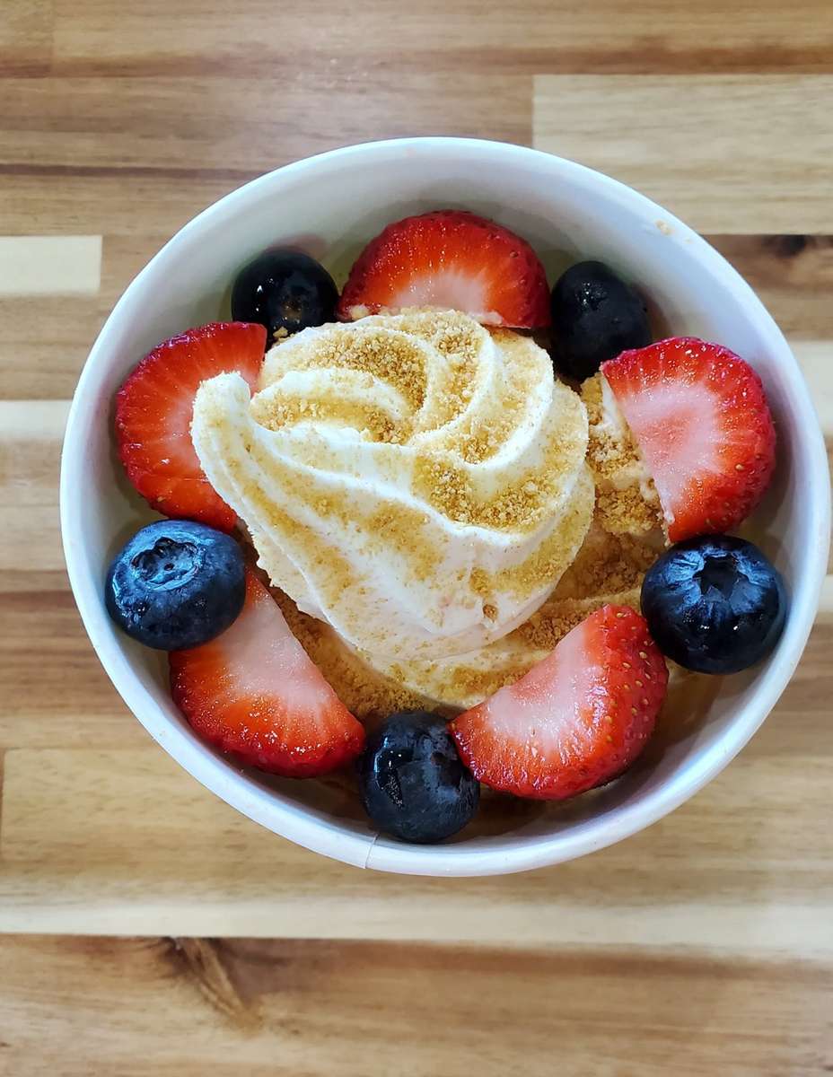 Heart-shaped vanilla soft serve topped with graham cracker crumble, fresh strawberries, and blueberries in a white bowl – romantic frozen yogurt dessert perfect for Valentine's specials at a dessert café.