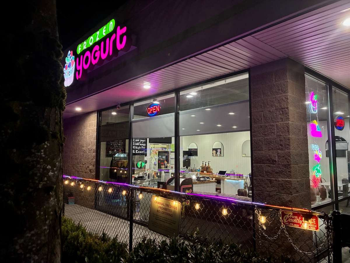 Exterior of a frozen yogurt shop at night with bright neon "Frozen Yogurt" signage, glowing open sign, and colorful window lights – modern dessert café storefront with inviting ambiance, perfect for a local ice cream or froyo business listing.
