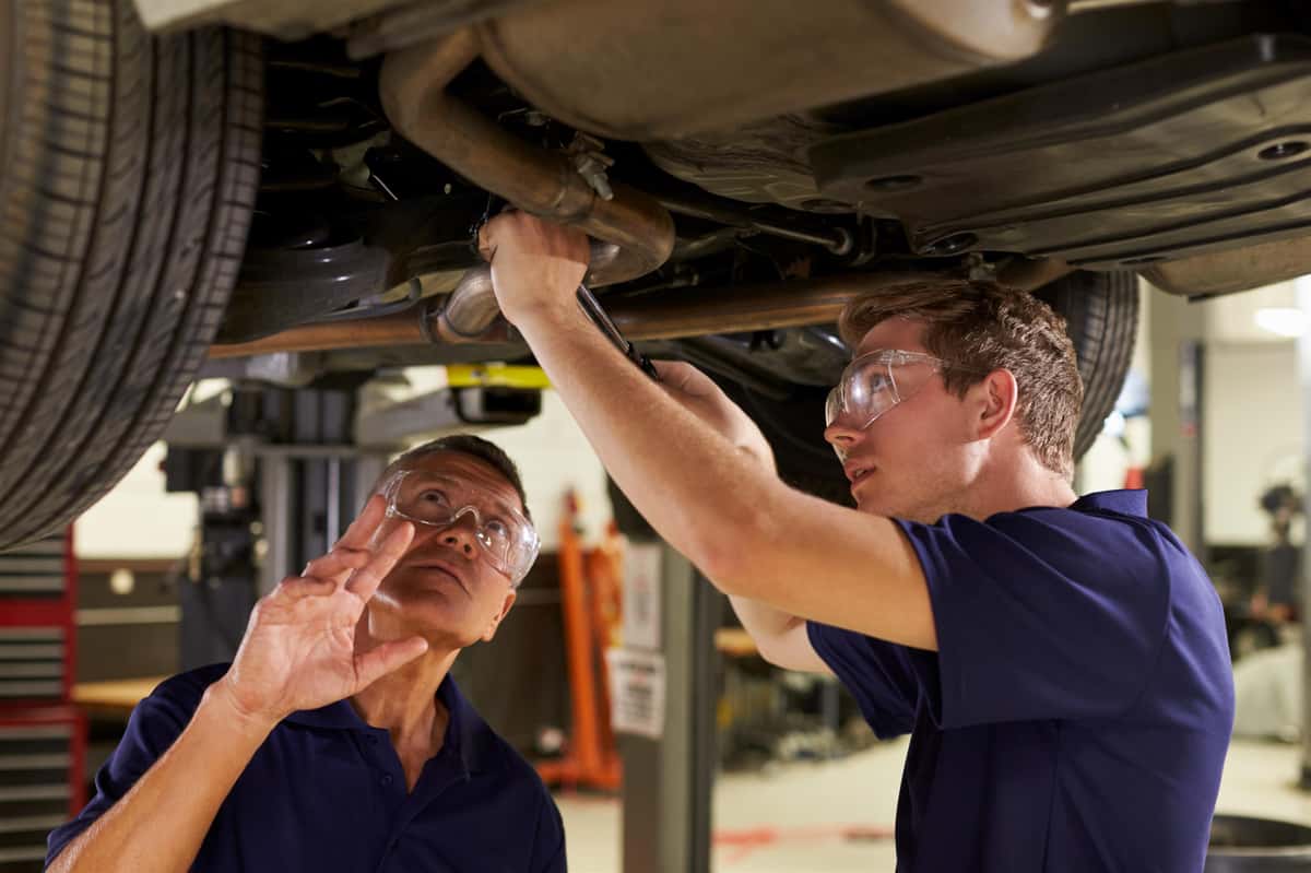 two mechanics wearing protective eye gear are looking at engine