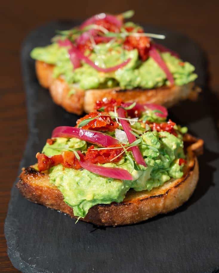 close up of avocado tartine toast topped with pickled onions