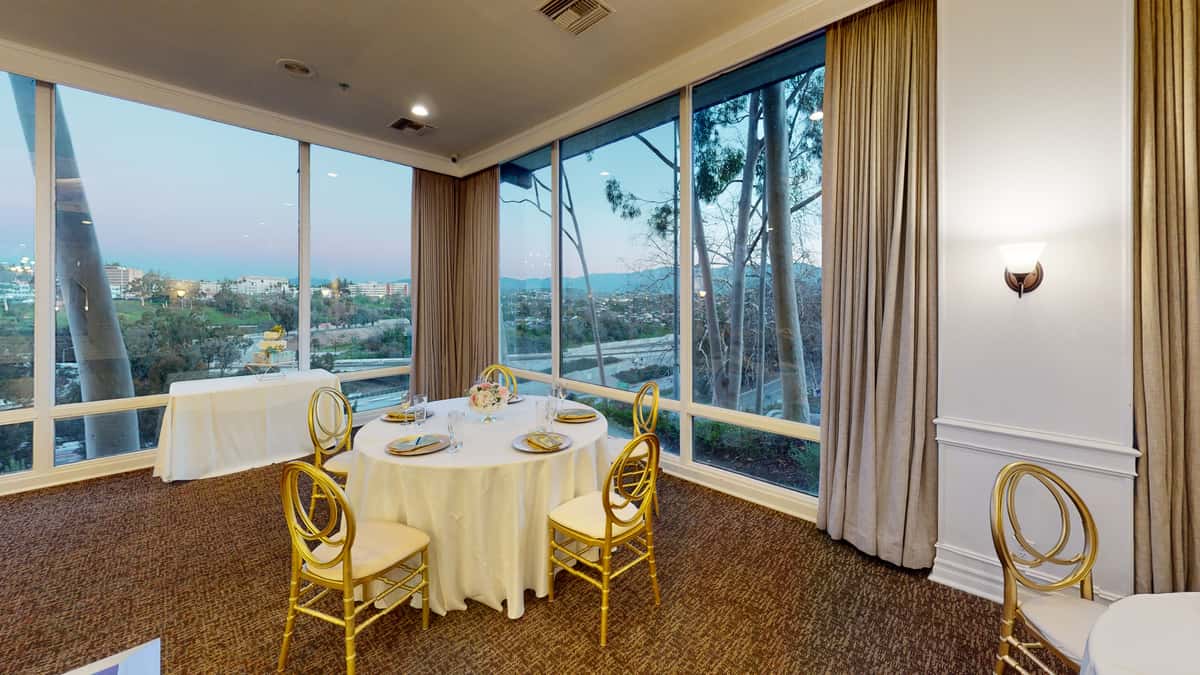 Private dining room with floor-to-ceiling windows, elegant round tables, and panoramic city views in an upscale event venue