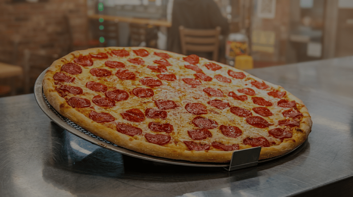 Large pepperoni pizza on a wire rack with a metal label holder, in a restaurant setting.