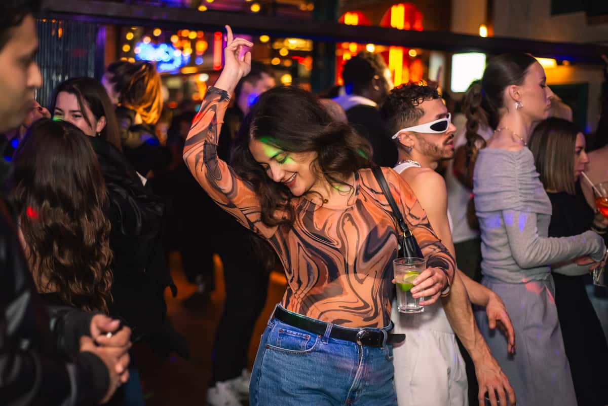 Girl on dancefloor with a drink in hand and the other one up