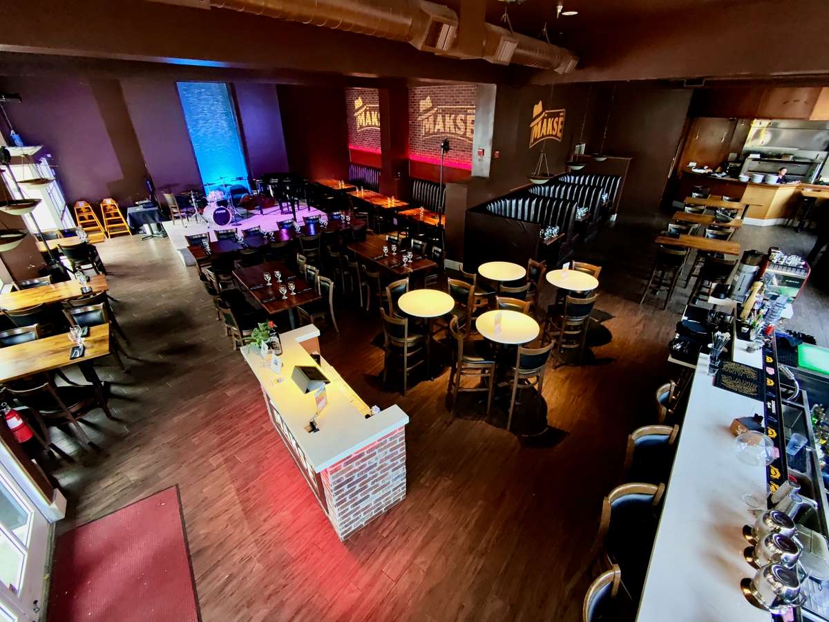 Modern restaurant and live music venue with stage, bar seating, dining tables, and private event space at Mäkse Restaurant.