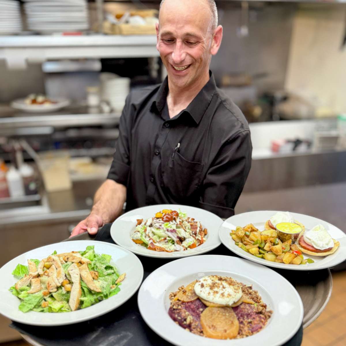 Chef holding freshly prepared lunch entrées featuring salads, grilled steak, and restaurant favorites in a commercial kitchen