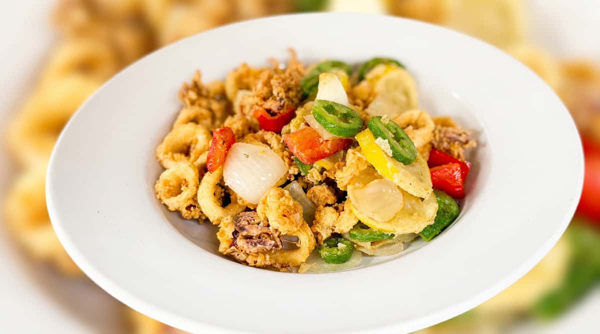Fried calamari with sautéed bell peppers, onions, yellow squash, and jalapeño slices on a white plate.