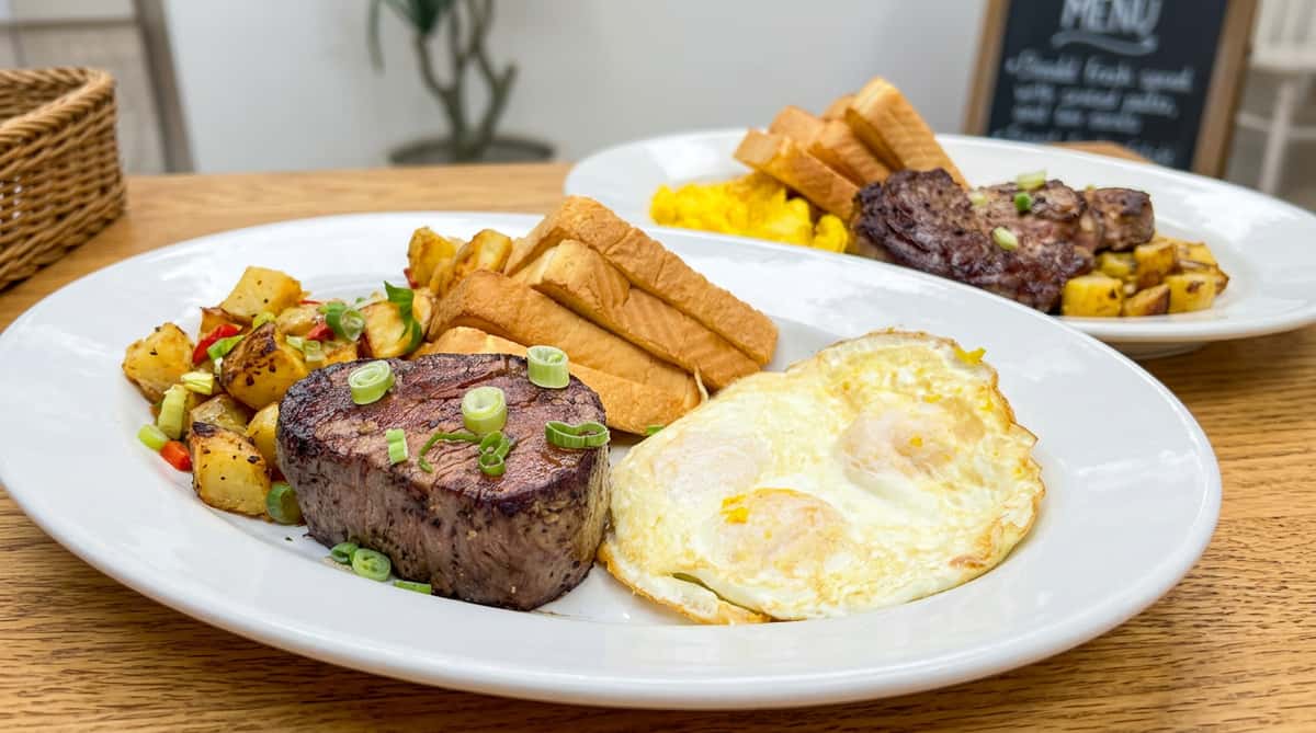 Full breakfast with steak, fried eggs, potato hash, and toast on a white plate.