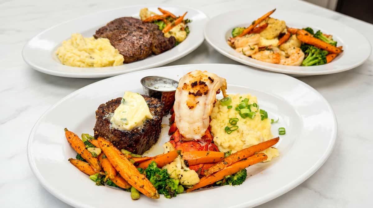 Grilled lobster tail and filet mignon topped with butter, mashed potatoes, and roasted vegetables.