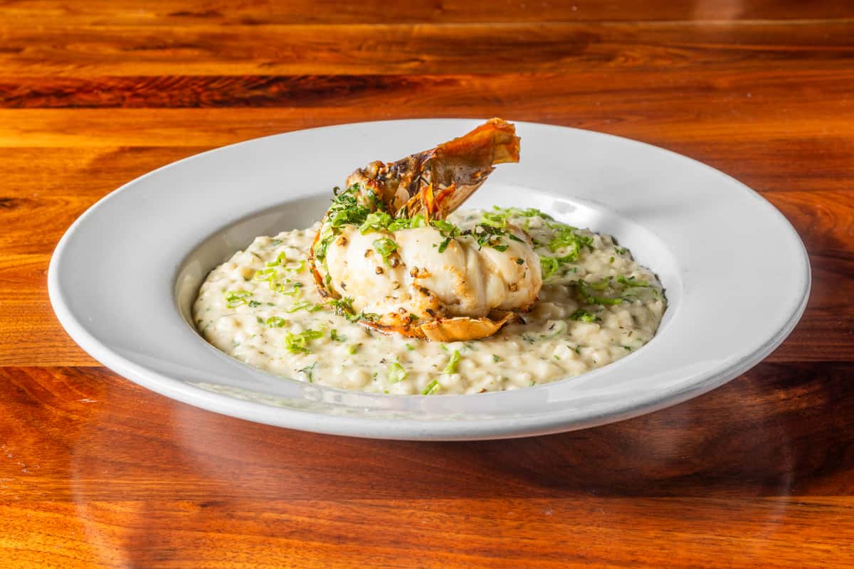 Grilled lobster tail served over creamy herb risotto and garnished with fresh herbs.