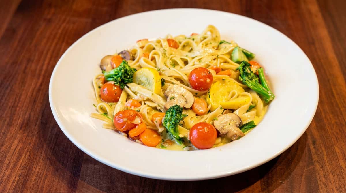 Linguine pasta with cherry tomatoes, broccoli, sliced carrots, mushrooms, and yellow squash in a cream sauce.
