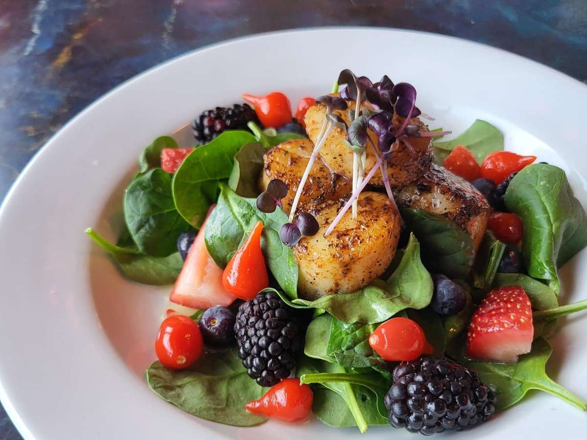 Seared scallops on a bed of spinach with blackberries, strawberries, blueberries, and cherry peppers, topped with microgreens.