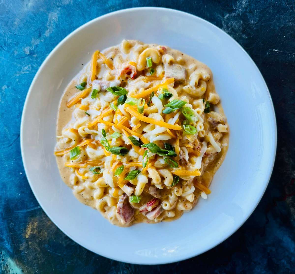 Creamy mac and cheese with chunks of sausage, topped with shredded cheddar and green onions on a white plate.