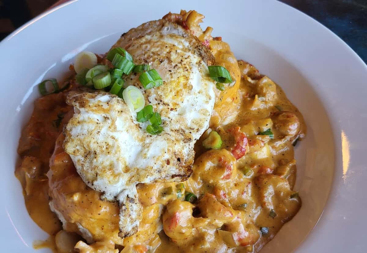 Crawfish étouffée over grits topped with a fried egg and garnished with chopped green onions.